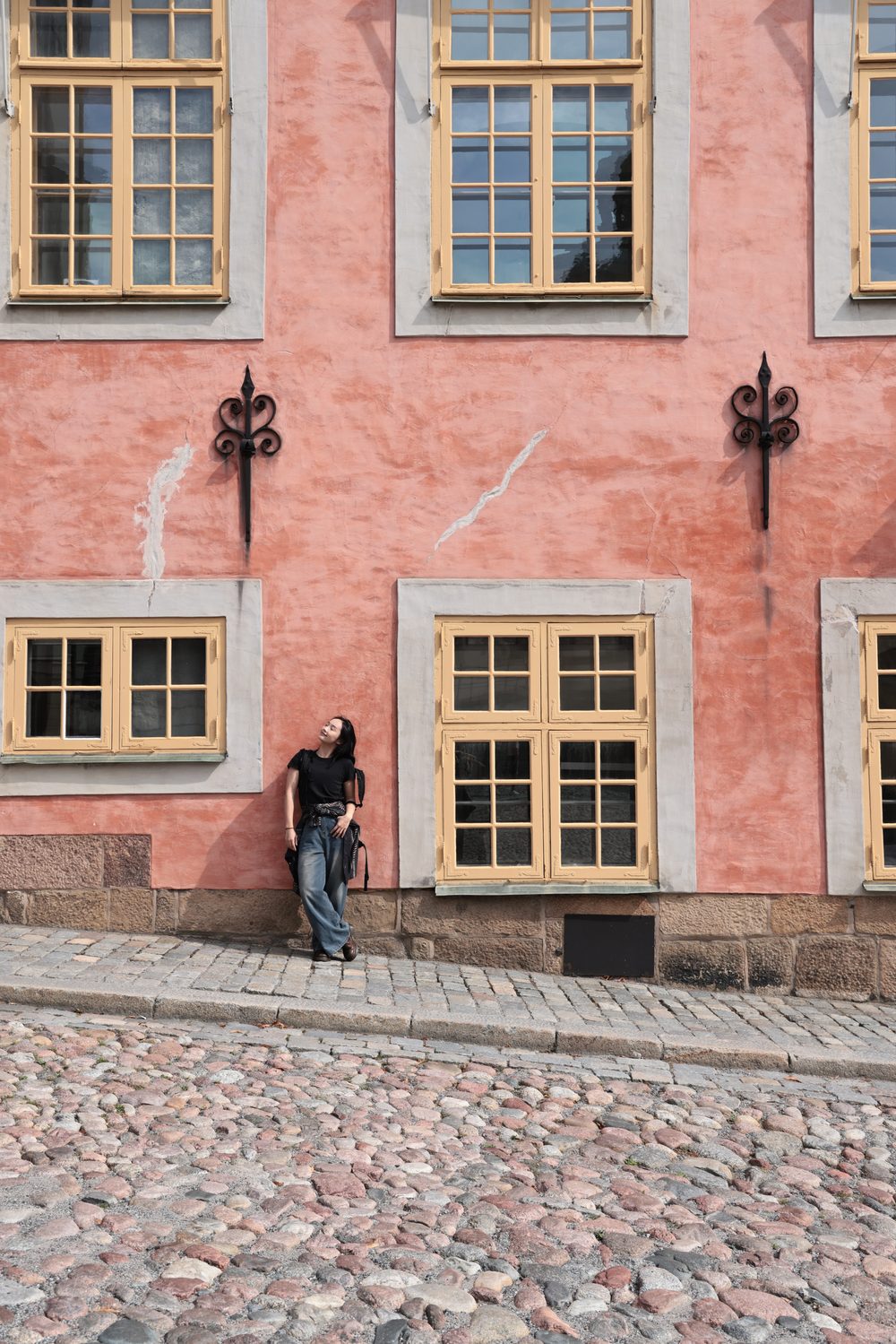 Leaning against a pink facade on the cobblestones