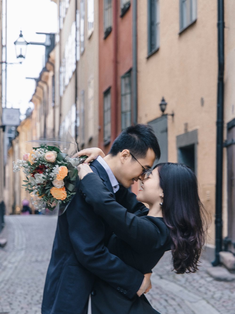 A couple embracing with a bouquet in an old town lane